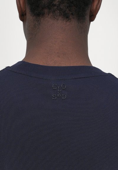 T-shirt bleu marine à manches courtes avec un col côtelé et un détail logo "CLOSED" en relief au dos, présentant une texture lisse.