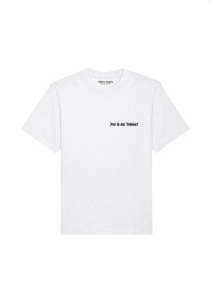 Jonge man met een wit T-shirt met de tekst "YOU & ME TONIGHT" op de borst en een blauwe spijkerbroek, staand tegen een effen achtergrond.