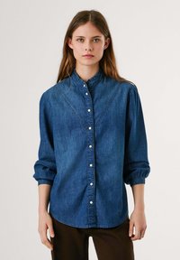 Dunkelblaue Denim-Bluse mit langen Ärmeln und Knopfverschluss. Sie verfügt über einen gerafften Kragen und dezente Nahtdetails über der Brust.