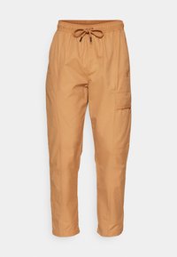 Pantalon cargo beige avec une taille élastique, un cordon de serrage ajustable, deux poches latérales et une poche passepoilée sur la jambe gauche. Texture de tissu lisse.