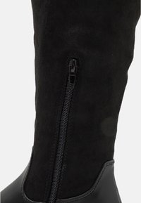 Botín negro hasta la rodilla con suela de cuero liso y parte superior de ante suave, con una cremallera lateral negra para el cierre.