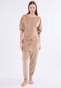 Beige geribbelde loungewear set met een losse top met opgerolde mouwen en broek met elastische taille. De stof heeft een zachte, gestructureerde uitstraling.