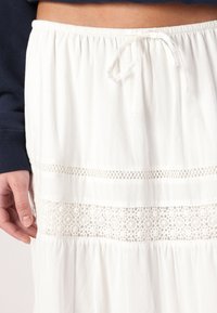 Vit kjol med elastisk midja och snörning, med intrikata spetsdetaljer längs den nedre delen, bärs med en marinblå långärmad topp.