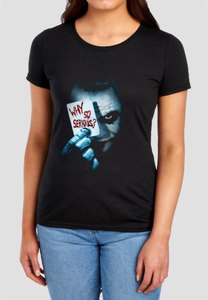 Person wearing black t-shirt with graphic of Joker's face holding "Why So Serious?" card in red text on front, paired with blue jeans.