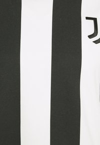 Sort-hvid stribet stof med V-hals design. Har et markant logo og ribbet tekstur på overfladen.