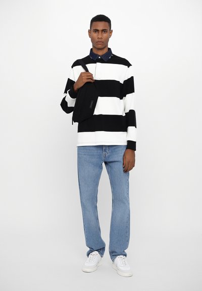 Black and white striped long-sleeve polo shirt, denim jeans, and white sneakers. Crossbody bag in black. Neutral background.
