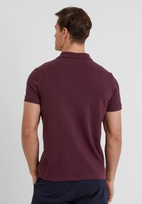 Maroon polo shirt made of cotton, featuring a classic collar, short sleeves, and a smooth texture. Back view shows a fitted design.