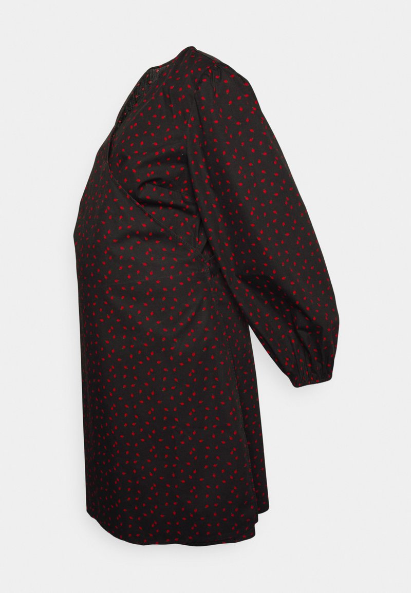 Vestido preto com bolas vermelhas. Apresenta mangas longas e bufantes, além de um corte solto. O tecido parece suave e leve.