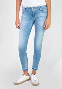 Lichtblauwe denim skinny jeans met een licht vervaagde afwerking, vijf zakken en een gouden knoopsluiting. Draagt met witte en grijze sneakers.
