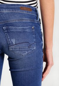 Mörkblå denimjeans med en lätt urtvättning, med en bakficka som har en subtil sömdesign och en brun läderetikett på midjebandet.