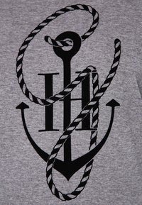 Grå t-shirt med en svart ankargrafik som är intrasslad i ett repmönster med stiliserad text, vilket betonar nautiska teman och textur.