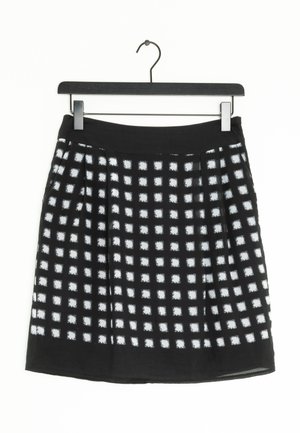Zwarte rok met wit ruitpatroon, gemaakt van zachte stof. Heeft plooien en een tailleband, hangend aan een zwarte plastic haak.