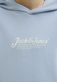 Felpa leggera blu chiaro in tessuto testurizzato. Presenta un logo frontale con testo bianco: "Jack & Jones", e dettagli di branding aggiuntivi qui sotto.