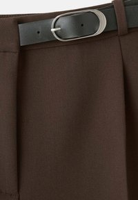 Pantalones marrones con un acabado texturizado, que presentan pliegues y un cinturón negro con una hebilla ovalada de plata. Enfóquese en un diseño elegante y ajustado.