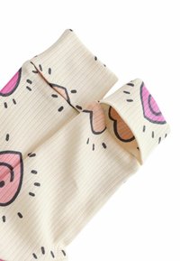 Ribbede creme farvede stoftop med pink og brune donut mønstre og sorte accenter, der har foldede ærmer. Designet inkluderer stiliserede perler.