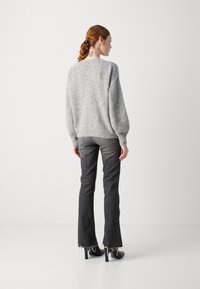 Maglione grigio in lana con un taglio morbido, maniche a sbuffo e un piccolo dettaglio a bottoni sul retro. Abbinato a jeans neri a campana e tacchi neri.