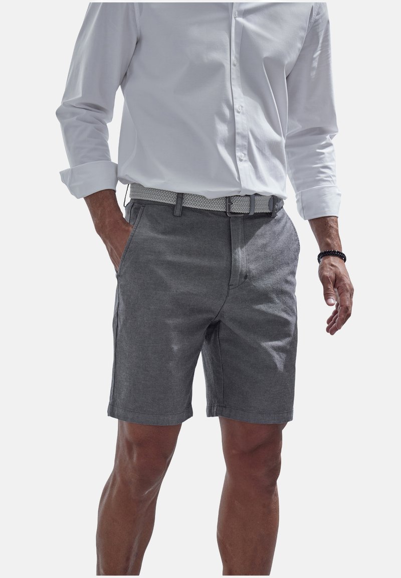 Graue Shorts aus leichtem Stoff, mit flachem Bund, Gürtelschlaufen und seitlichen Taschen. Kombiniert mit einem weißen Langarmshirt.