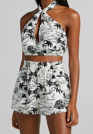 Top sin mangas en blanco y negro con un diseño de abertura en el pecho, que presenta un estampado de palmeras y flores; combinado con pantalones cortos de cintura elástica a juego.