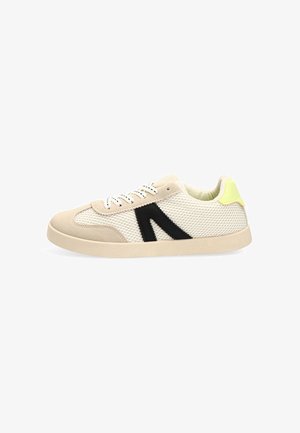 Zapatilla de malla beige y blanca con detalle lateral negro, cordones blancos y acento amarillo en el talón, mostrada de lado sobre un fondo blanco.