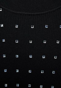 Tessuto a maglia nero a coste con accenti di cristalli metallici quadrati disposti in un pattern a griglia sulla superficie.