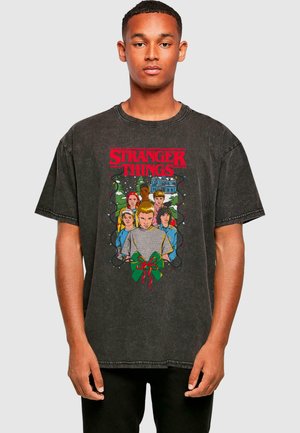 Black oversized t-shirt featuring a colorful "Stranger Things" graphic with characters and a holiday bow, made of cotton with a worn finish.