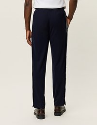 Námornícke športové nohavice s voľným strihom, s bočnými zipsami a hladkou textúrou. Nosené s hnedými topánkami a bielou košeľou.