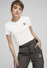 Hvid kort t-shirt med sort Puma-logo på venstre bryst, parret med teksturerede mørkegrå joggers med et gentaget fiskebensmønster.