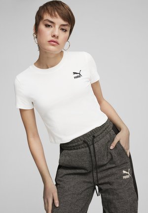 Maglietta bianca a maniche corte con logo Puma nero sul lato sinistro del petto, abbinata a pantaloni joggers grigio scuro con texture e un motivo a spina di pesce ripetuto.