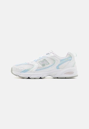 Zapatilla New Balance 530 blanca y azul claro con capas de malla y sintéticas, cierre de cordones y suela acolchada visible desde un lado.