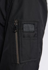 Giacca nera con tasca con zip e etichetta intrecciata, tessuto testurizzato e dettagli in zip a contrasto. Design semplice e funzionale.