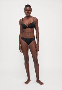 Černý bikini set se sukní s tvarovanými košíčky, nastavitelnými ramínky a odpovídajícími nízko posazenými kalhotkami, vyrobený z hladké, elastické tkaniny.