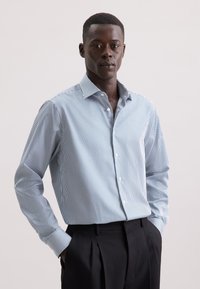 Button-up shirt met verticale blauw-witte strepen, lange mouwen en een klassieke kraag. G gedragen met zwarte broek.