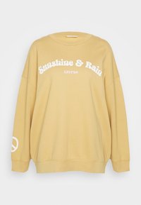 Sudadera amarilla de gran tamaño con texto blanco "Sunshine & Rain" y un símbolo de paz en la manga. Material suave con cuello redondo acanalado.