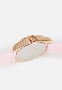 Montre avec un bracelet en silicone rose et un boîtier en acier inoxydable doré rose. Possède une couronne texturée et un cadran de montre en argent poli.