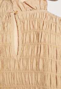 Tissu beige froncé avec des coutures rassemblées horizontales et une petite fermeture à bouton au niveau d'un détail en trou de serrure.