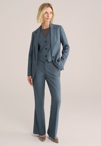 Costum cu trei piese, care include un sacou ajustat, o vestă și o pereche de pantaloni dintr-un material albastru discret. Textură netedă, design ajustat, cu buzunare frontale.