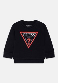 Svart bomullssweatshirt med rødt trekantlogo. Har trykknapper på skulderen og ribbestrikkede mansjetter. Teksten inkluderer "GUESS," "U.S.A.," og "WASHED JEANS."