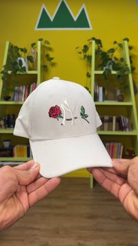 White baseball cap featuring embroidered red rose and leaf design, with a raised white NY logo, textured fabric, and curved brim.