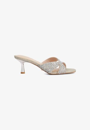 Sandale mule argentée à bout ouvert avec un talon fin de hauteur moyenne et des brides croisées recouvertes de strass scintillants.