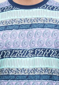 Μπλουζάκι με πολύχρωμες οριζόντιες ρίγες που απεικονίζουν στροβιλισμένα σχέδια, σειρές από χορεύοντας χαρακτήρες με μπάλα 8, και το κείμενο «Santa Cruz».