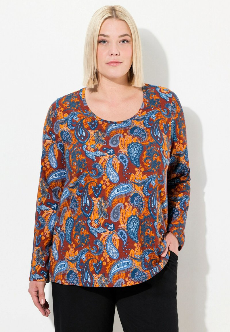 Langärmliges Oberteil mit Paisleymuster in orange, blau und braun; runder Ausschnitt und lässige Passform. Kombiniert mit schwarzen Hosen.