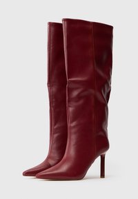 Botas de cuero burdeos altas con puntas afiladas y tacones altos delgados, mostradas lado a lado sobre un fondo blanco liso.