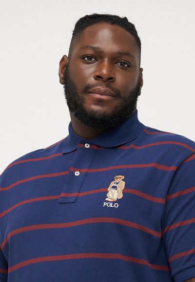 Marineblauwe poloshirt met rode strepen, voorzien van een geborduurd berenlogo op de linkerborst. Gemaakt van gestructureerd katoenmateriaal.