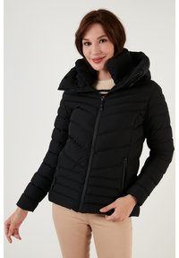 Black puffer jacket with a high collar and a zip front. It features chevron quilted detailing and two side pockets.