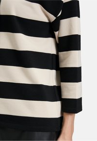 Czarna i kremowa bluzka z długim rękawem w paski, charakteryzująca się miękką fakturą, luźnym krojem oraz mankietami na rękawach, z prostym dołem.