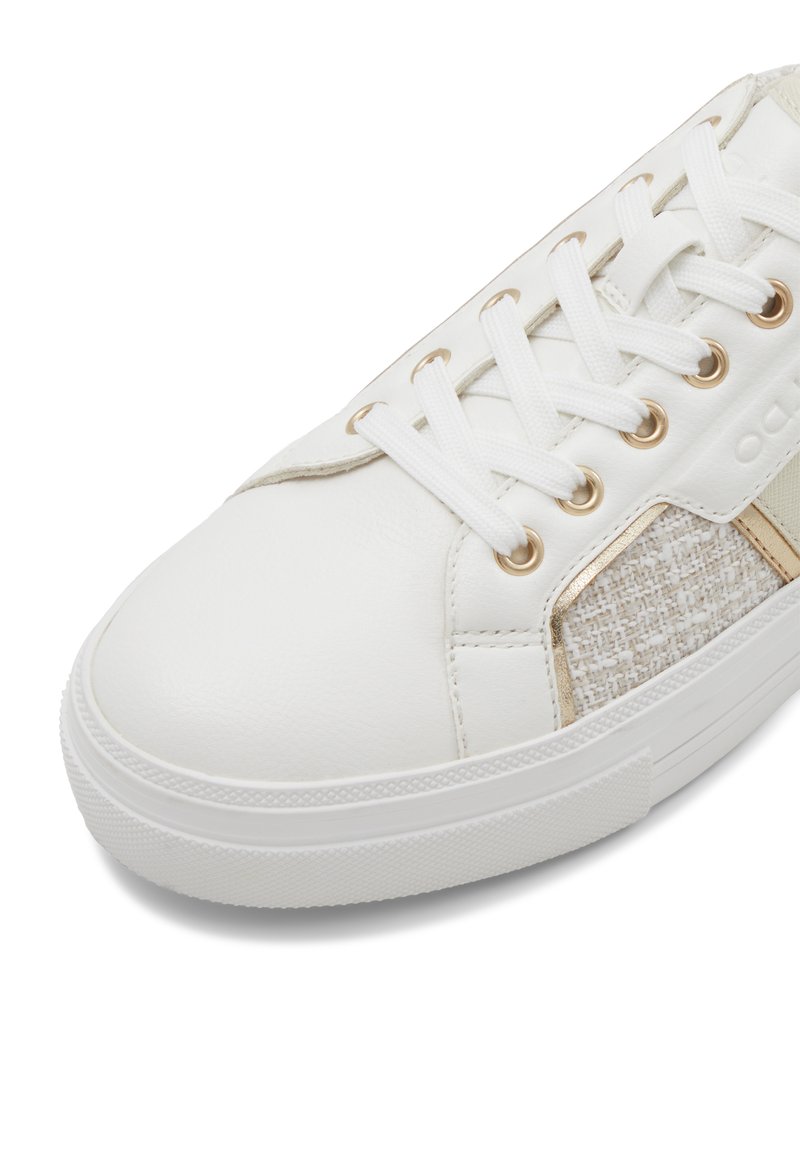 Zapatilla blanca con un acento beige texturizado. Las características incluyen un empeine de cuero suave, ojetes dorados y cordones planos blancos.