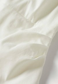 Gros plan sur un tissu lisse blanc cassé avec des coutures subtiles et des plis doux créant de légères ombres à la surface.
