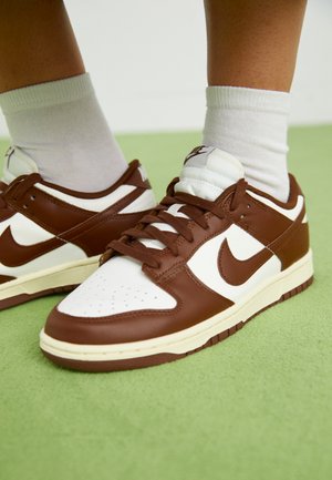 Braune und weiße Leder-Sneaker mit perforierter Zehenpartie, strukturierten Akzenten und flachen Schnürsenkeln. Das Modell hat ein Low-Top-Design und eine Gummisohle.