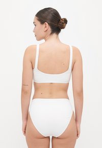 Wit bikini set met een eenvoudige bralette top met dunne bandjes en een hooglab hoezebroekje. Gladde textuur en minimalistisch ontwerp.