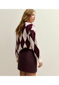 Maglione con motivo argyle bordeaux e bianco, texture a maglia e polsini a costine, abbinato a una gonna aderente in ecopelle bordeaux.